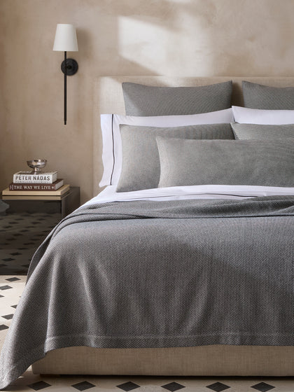 Jackson bedding in grey herringbone weave, styled in a bedroom with a wall sconce and tiled floor