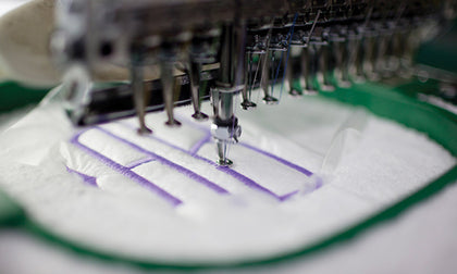 Close-up of an embroidery machine stitching a monogram onto white linen.