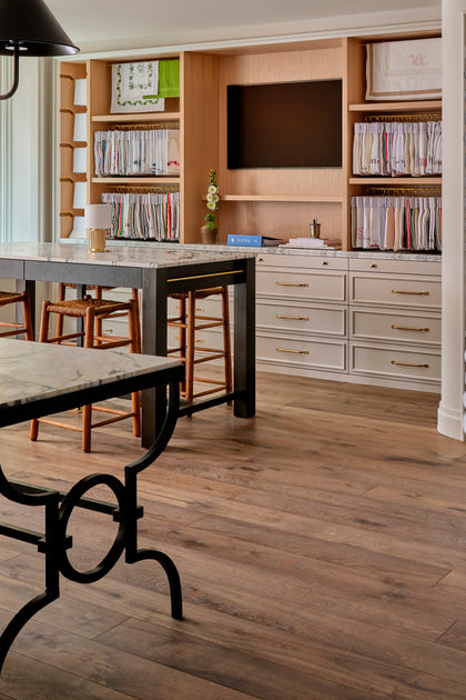 Interior of a design studio with marble-top tables, wicker stools, and open shelving displaying folded linens.