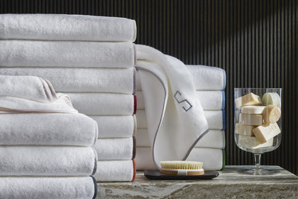 Stack of Giza towels with contrast piped trim, soap, and a brush.