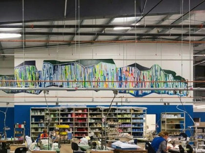 Matouk factory floor with thread shelves, a wall mural, and seamstresses sewing linens.