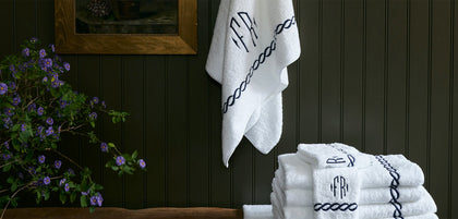Round block-letter monogram with a chain-link border on bath towels.