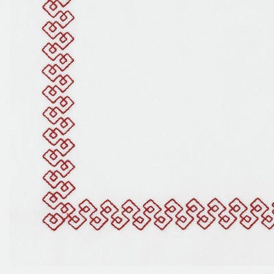 Close up of a napkin with a red geometric border pattern along the top and left edges, leaving the center blank.