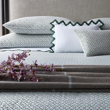 Sage medallion-print bedding with a dark green scalloped pillow and plaid throw