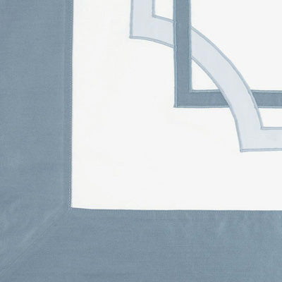 Close up of a napkin featuring a dusty slate blue border and a matching geometric border design in the top right corner.