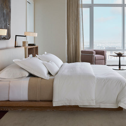 Hotel bedroom styled with crisp white bedding and floor-to-ceiling city views
