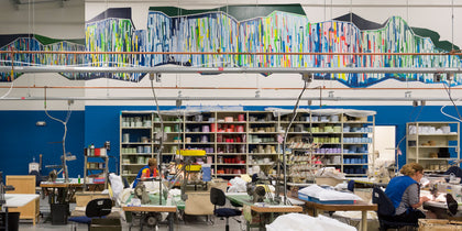 Factory floor with sewing stations, thread shelves, and a mural