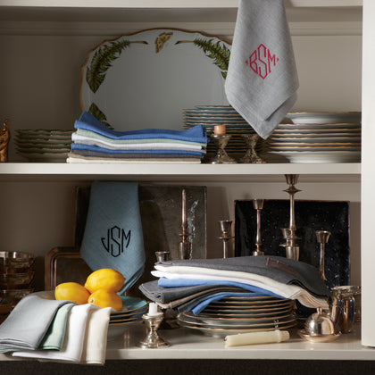 Monogrammed Chamant linens on an open shelf with silver candlesticks and china