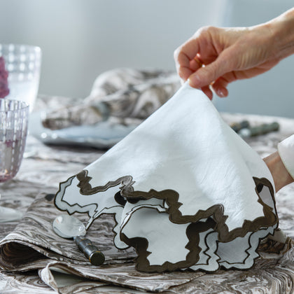 Hand lifting Aziza scalloped napkin above a Balthazar marbled table.