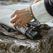 Hand holding Aziza's scalloped napkin edge over Balthazar marbled linen.