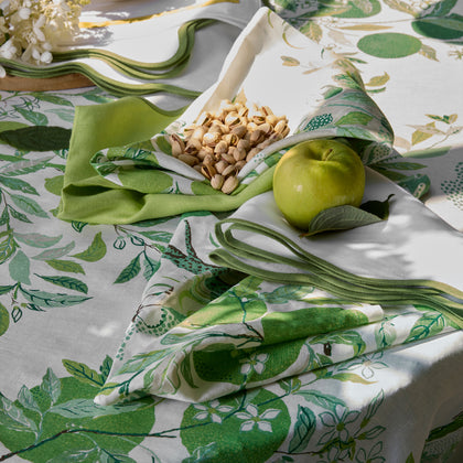 Green Citrus Garden leaf-print tablecloth and napkins set with an apple and pistachios.