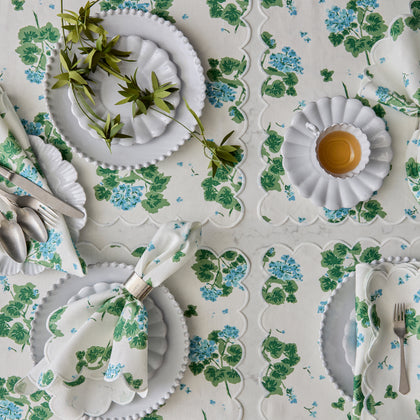 Blue and green Geranium print table linens set with scalloped placemats and white china.