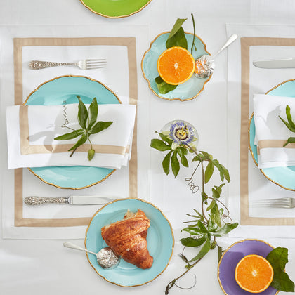 White Lowell tan-bordered placemats set with turquoise plates, croissants, and citrus.