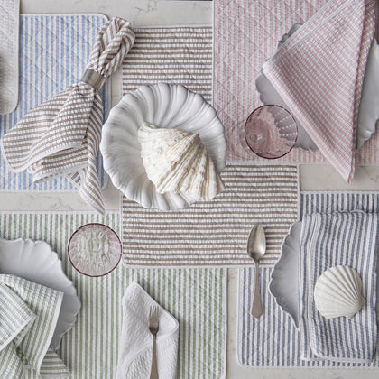 Matteo striped placemats in blue, pink, tan, and green, set with scalloped plates and seashells.