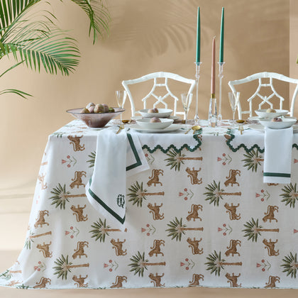 Tiger Palm print tablecloth with tigers and palm trees, styled on a table with bamboo chairs, candles, and green-trimmed monogrammed napkins.