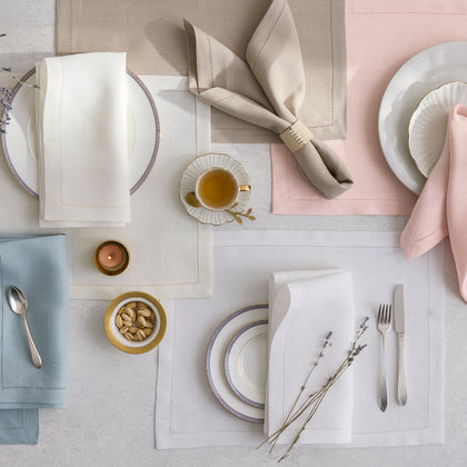 Valentina Hemstitch linen placemats and napkins in pastel colors, arranged flat with china.