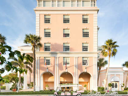 A tall peach-pink hotel building with white trim, palm trees, blue sky, and a pink golf cart in front.