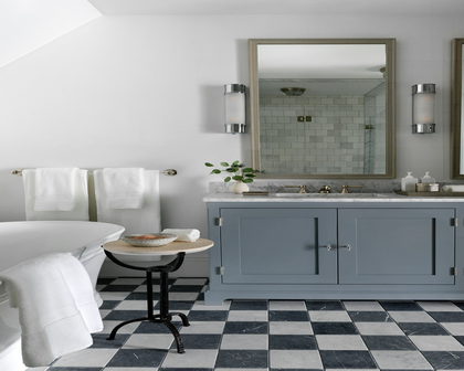 A styled bathroom interior featuring a light blue double-sink vanity cabinet with a white marble countertop, a large wood-framed mirror, black-and-white checkered flooring, and white towels.