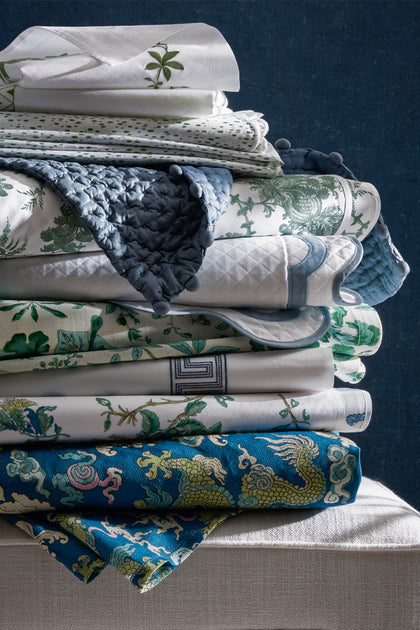 Stack of Schumacher Matouk collaboration linens, including the Magic Mountain dragon print, in blue and green