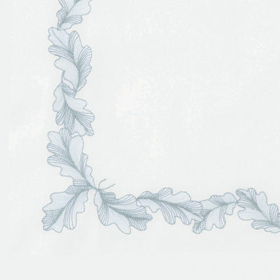 Close up of a napkin featuring a delicate, light blue-gray embroidered oak leaf border along the left and bottom edges.