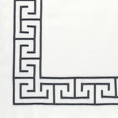 A close-up of a white fabric or material corner featuring a black Greek key geometric border pattern.