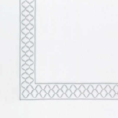 A close-up of a white sheet with a decorative border featuring a repeating interlocking geometric pattern in light gray along the left and bottom edges.