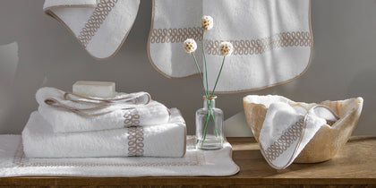 White towels with a tan embroidered loop trim, stacked and hanging.