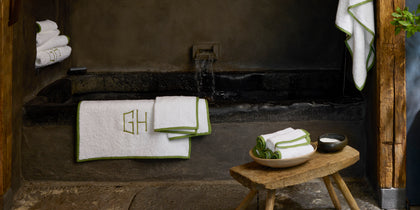 White monogrammed towel with a green trim, in a stone bathroom.