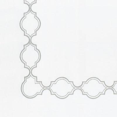 Close up of a napkin with a light gray repeating quatrefoil or trellis border pattern along the left and bottom edges.