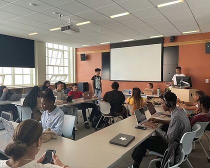 College Visions students in a Rhode Island classroom working on laptops as a peer presents at the front of the room