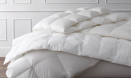 Close-up of a plush white down comforter draped over a bed.