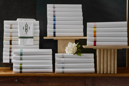 Stacked white sheet sets with colorful satin border trims and a monogrammed towel