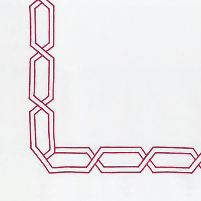 Close up of a napkin featuring a decorative red embroidered geometric corner pattern.