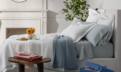 Light blue bedding styled on a bed with a gift box.