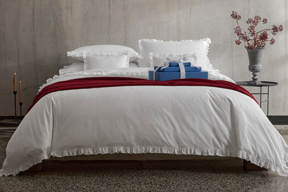White ruffled bedding with a red throw and a gift box.