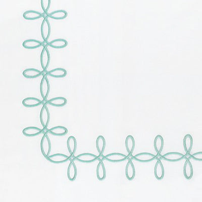 Close up of a napkin featuring a mint green embroidered decorative border with a repeating looped floral pattern