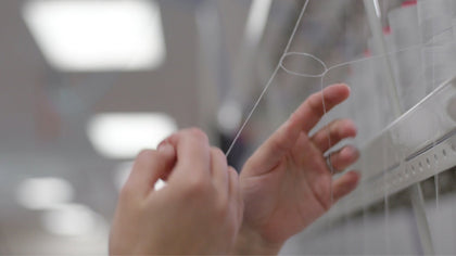 Close-up of a person's hands holding and stretching a thin transparent string or cord in front of a blurred indoor background with bright ceiling lights.