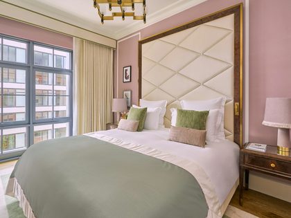 Luxury hotel bedroom with tufted cream headboard, sage green bedding, blush pink walls and brass chandelier