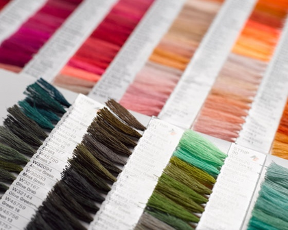 A close-up of a fabric or thread color swatch card showing multiple vertical strips of different colors, including pink, orange, yellow, green, brown, and teal, with printed labels visible on the white card.