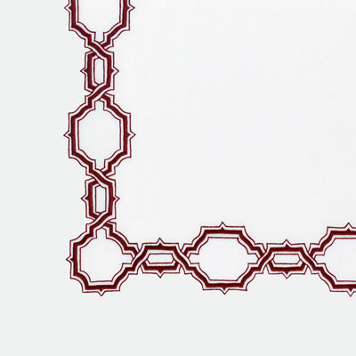 Close up of a napkin featuring a geometric patterned corner detail, showing interlocking ornate links in a deep burgundy red color