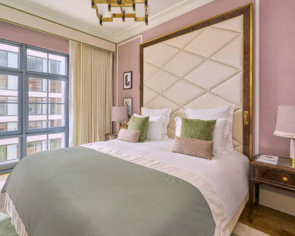 Luxury hotel guest room with diamond-tufted headboard in a burl wood and brass frame, blush walls and sage bedding