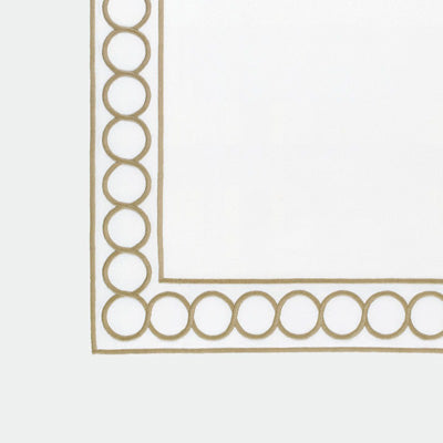 Close up of a napkin featuring a gold border design with repeating interlocking circle motifs along the left and bottom edges.
