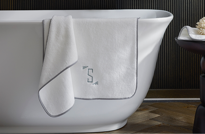 Monogrammed white towel with gray trim draped on a freestanding tub