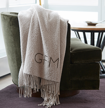 Monogrammed ivory fringed throw draped over a green velvet armchair