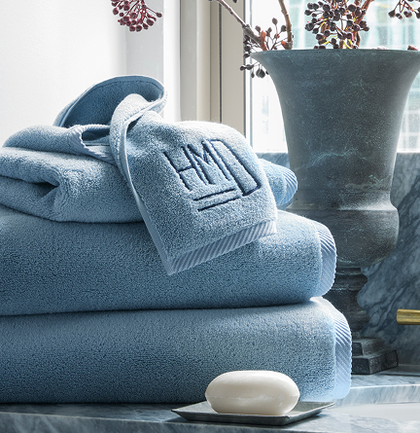 Stack of monogrammed blue towels on a marble ledge with a vase