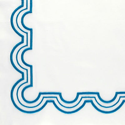 Close up of a napkin with a blue scalloped embroidered border