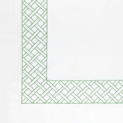 Close up of a napkin featuring a green embroidered basketweave pattern along the border, with the corner turned up to reveal a solid white center.