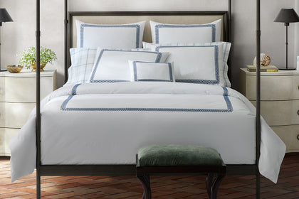 White Astor Braid bedding with a navy embroidered border, styled on a bed.