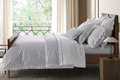 White Celine bedding with a navy scalloped trim, styled on a bed.