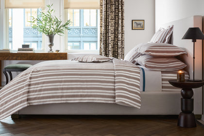 Brown striped Elio bedding styled on a bed.